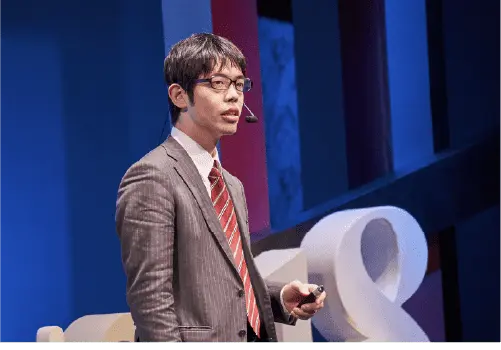 A man in a suit and headset is presenting.
